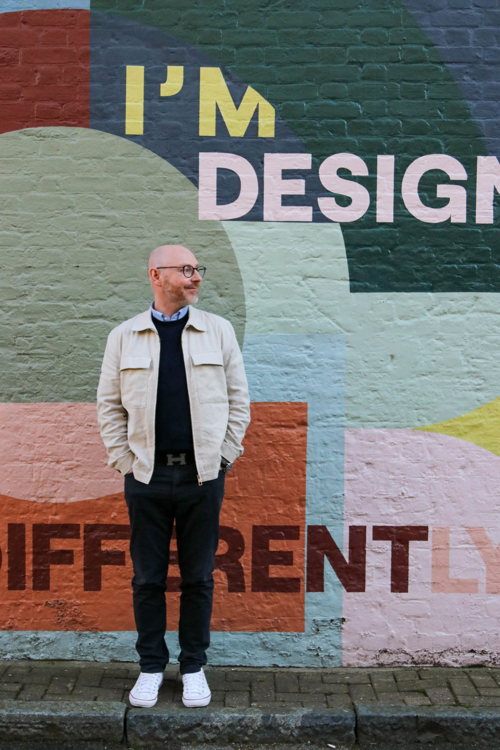 Tom Foulkes, former head of brand at McLaren and current managing director of HB, stands against a lively, colourful backdrop.